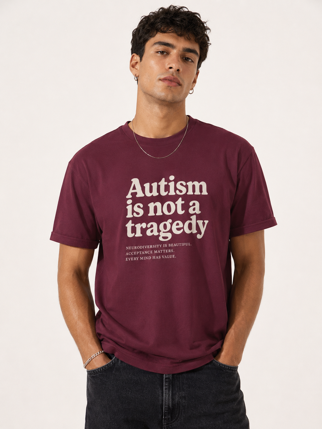 Man wearing a maroon t-shirt with 'Autism is not a tragedy' text on a plain background