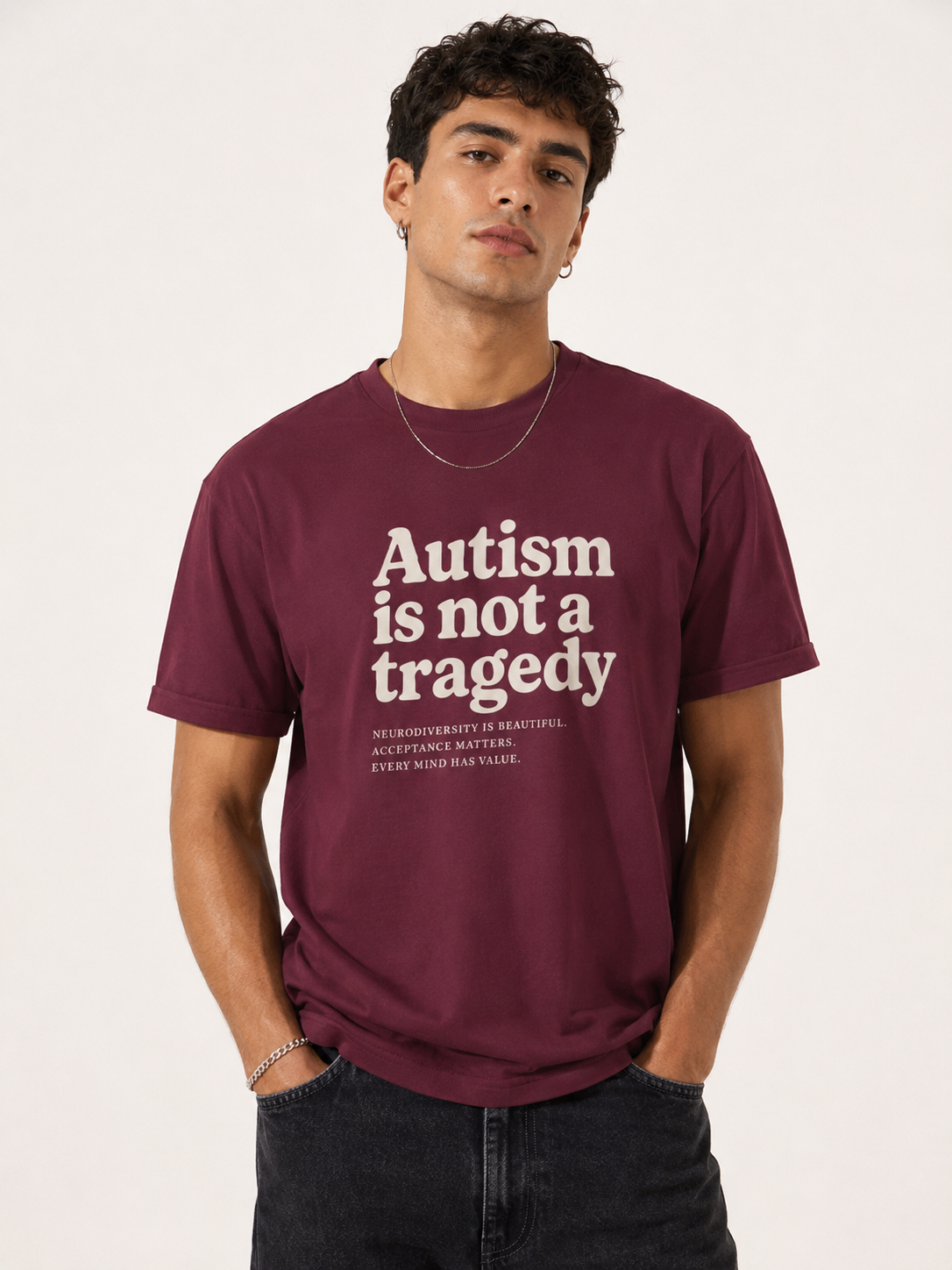 Man wearing a maroon t-shirt with 'Autism is not a tragedy' text on a plain background