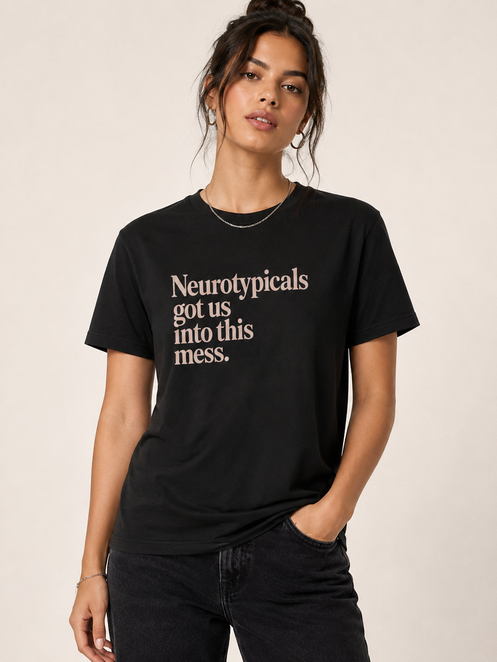 Person wearing a black t-shirt with text, standing against a plain background text is rose colored and reads Neurotypicals got us into this mess.