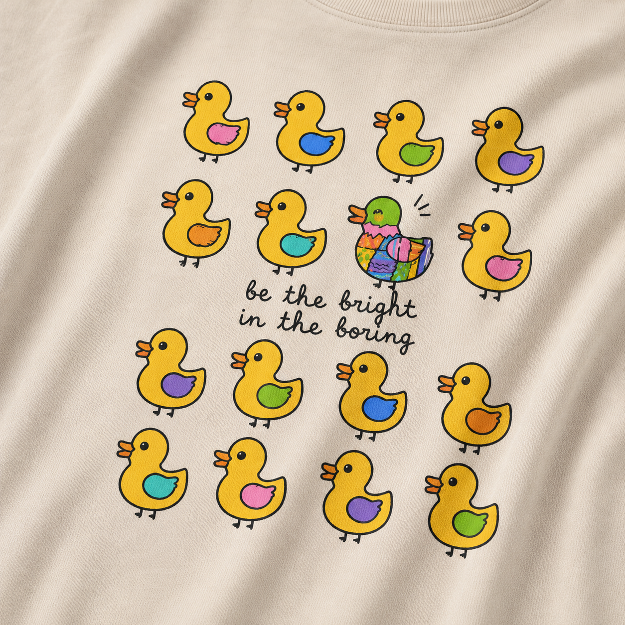 Beige t-shirt with colorful duck illustrations and a central message.