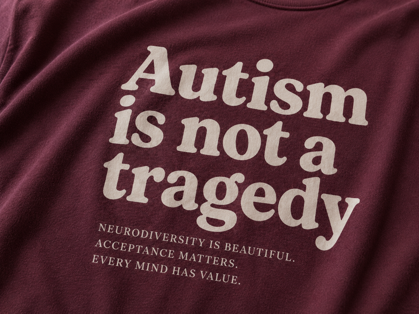 Maroon t-shirt with white text 'Autism is not a tragedy' and supporting messages.