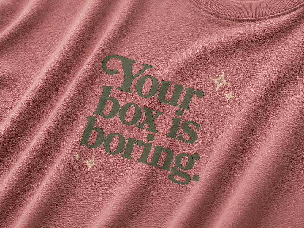 Mauve t-shirt  with green text 'Your box is boring.' and star graphics.