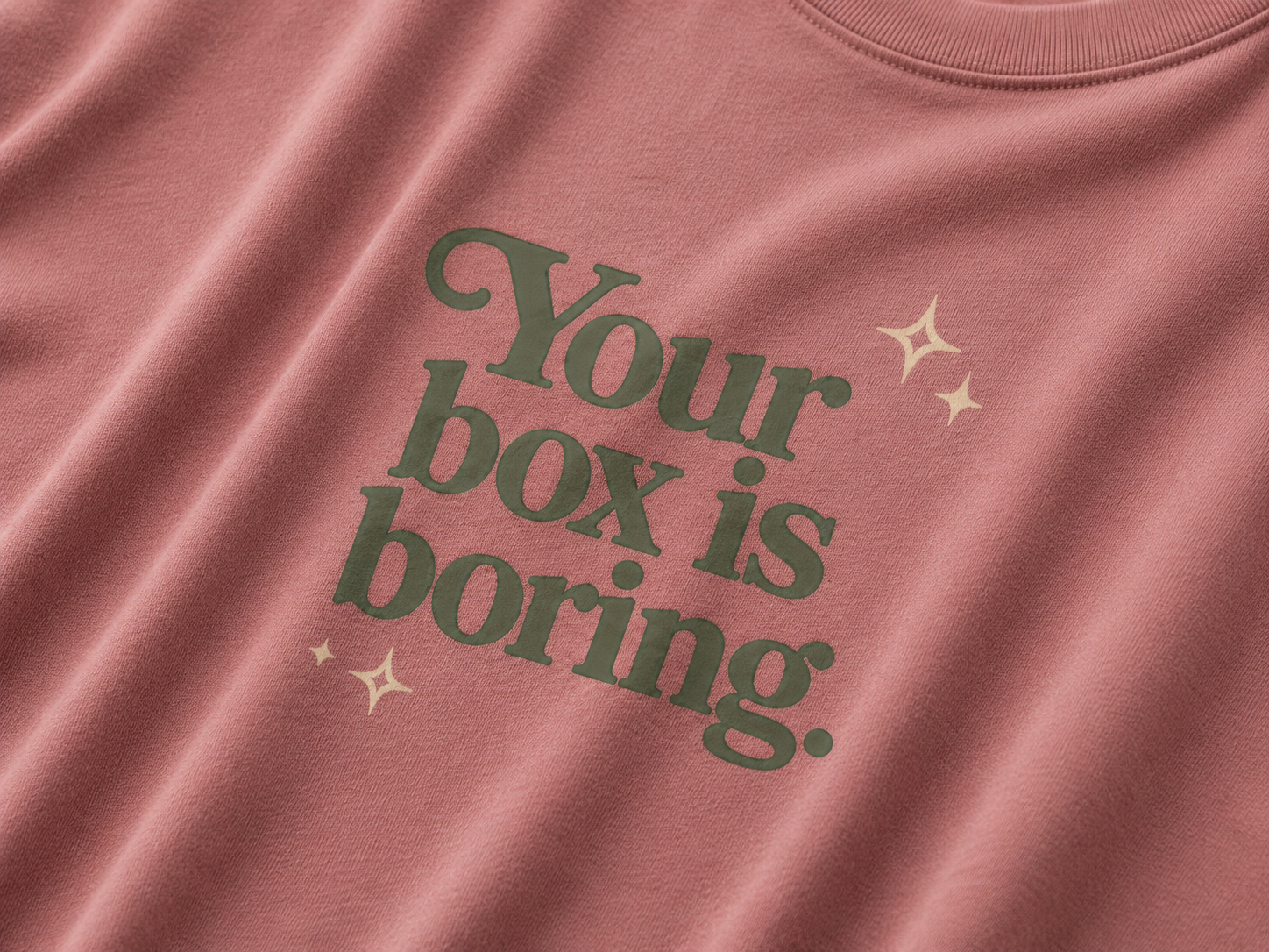 Mauve t-shirt  with green text 'Your box is boring.' and star graphics.