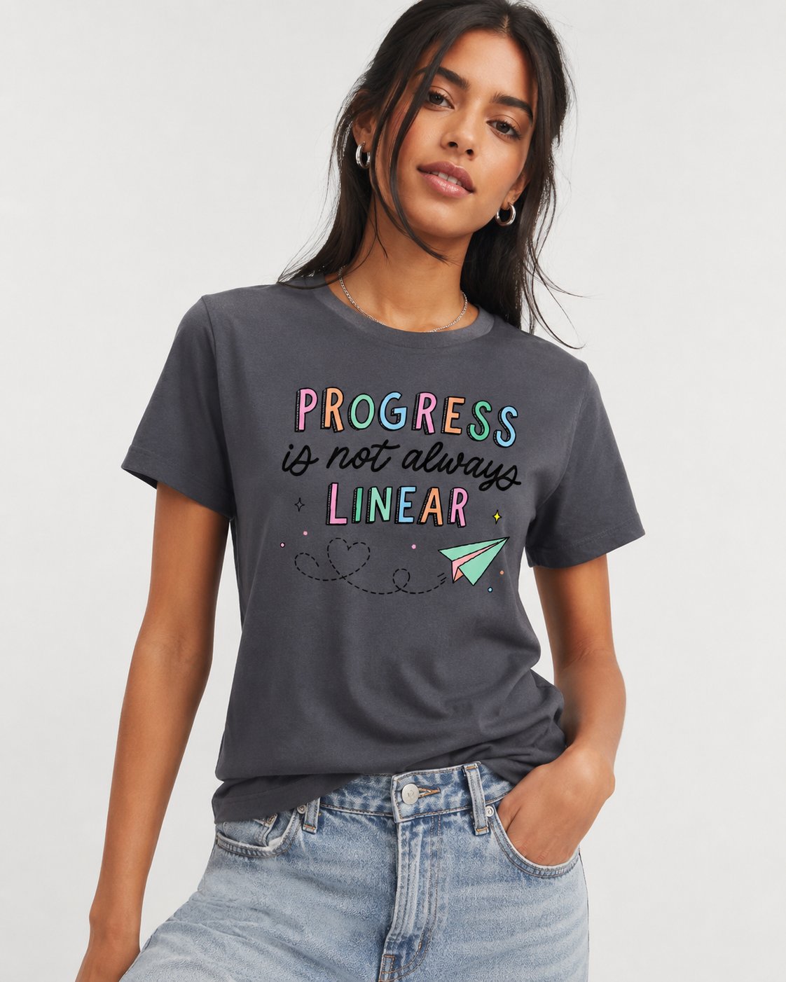 Person wearing a dark gray t-shirt with colorful text and a paper airplane graphic on a plain background text says Profress is not always linear