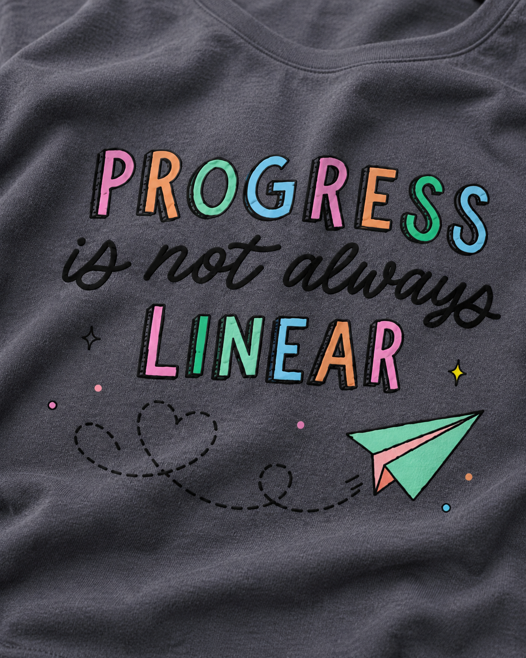 Gray t-shirt with colorful text 'PROGRESS is not always LINEAR' and a paper airplane graphic.