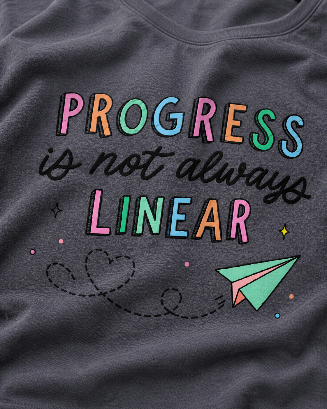 Gray t-shirt with colorful text 'PROGRESS is not always LINEAR' and a paper airplane graphic.