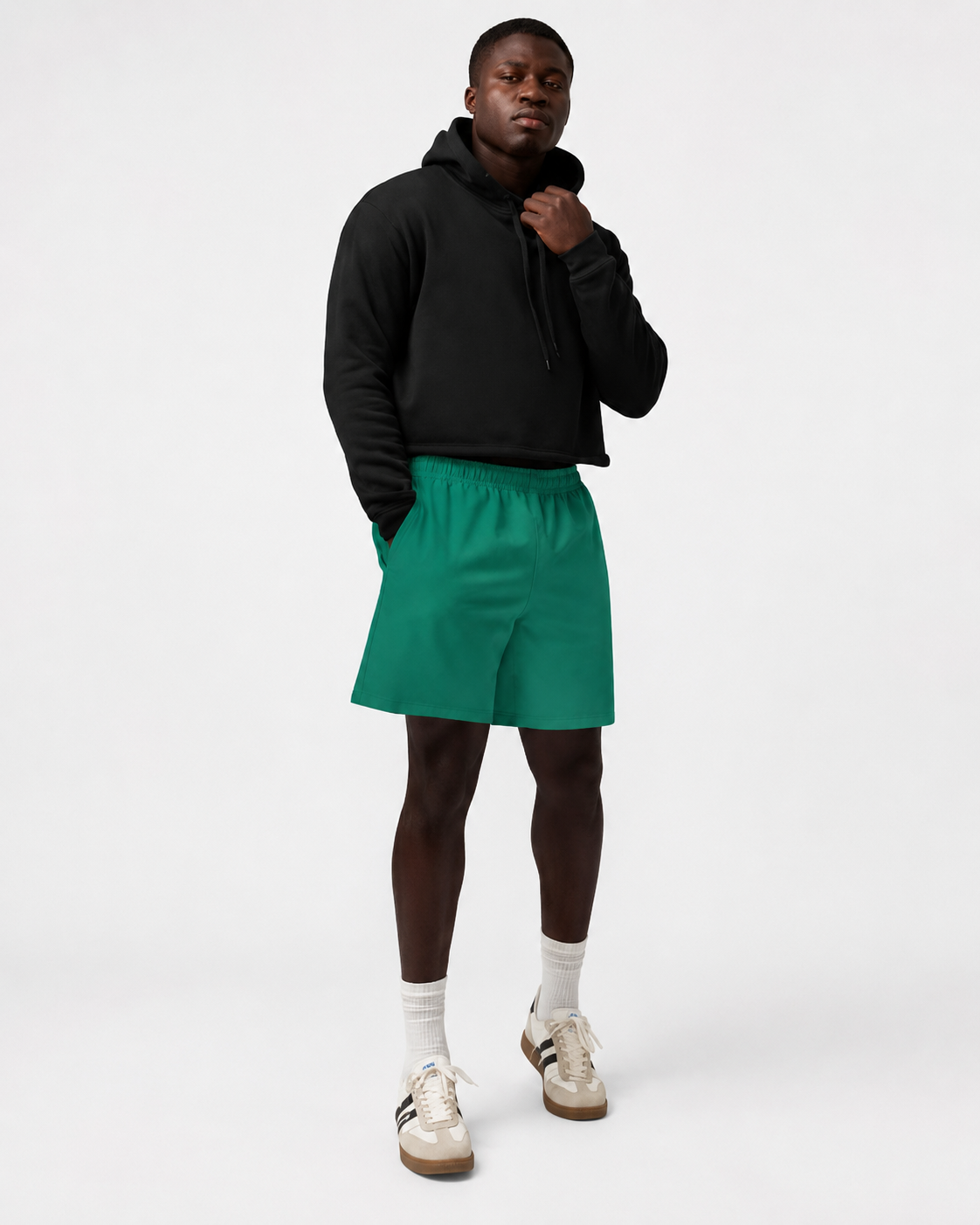 Person wearing a black hoodie and green shorts on a white background